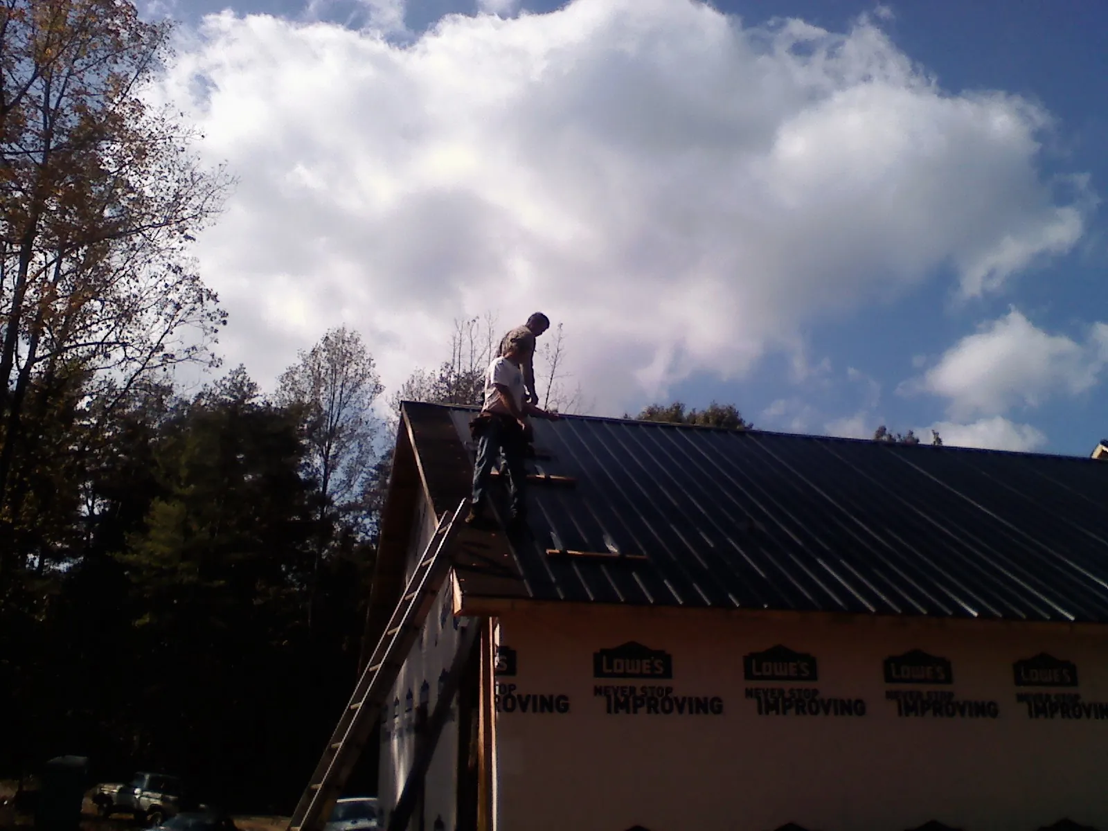 Roofer fastening dark metal panels high against a cloudy sky, from a Roof Inspection job in Barnesville